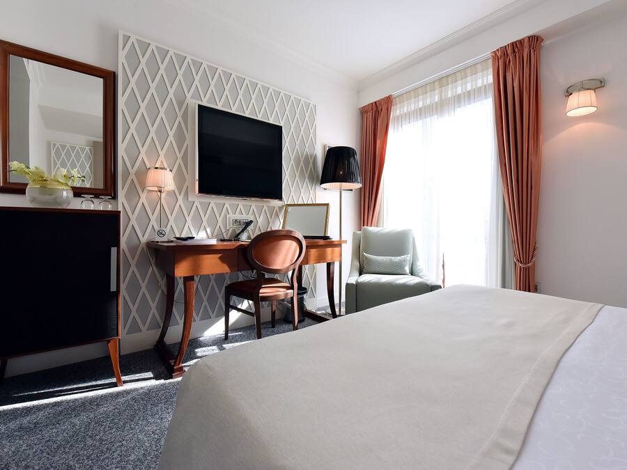 A hotel room with a bed, a desk, a chair, a TV, and a lamp.
