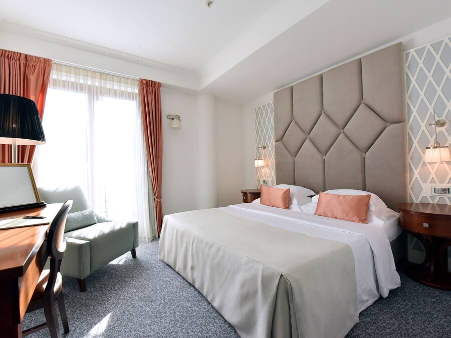 A hotel room with a bed, a desk, a chair, a lamp, and a nightstand.