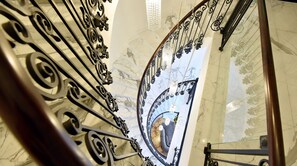 A marble staircase with ornate black metal railings and a chandelier.