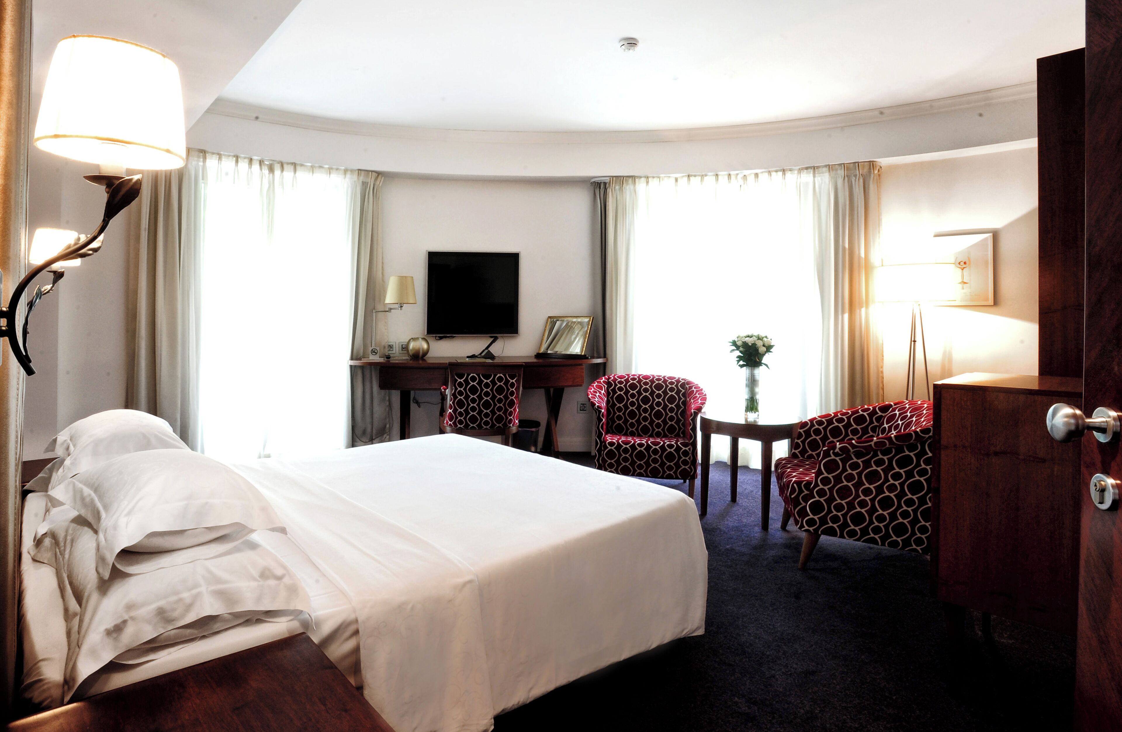 A hotel room with a bed, two armchairs, a desk with a TV, and a dresser.