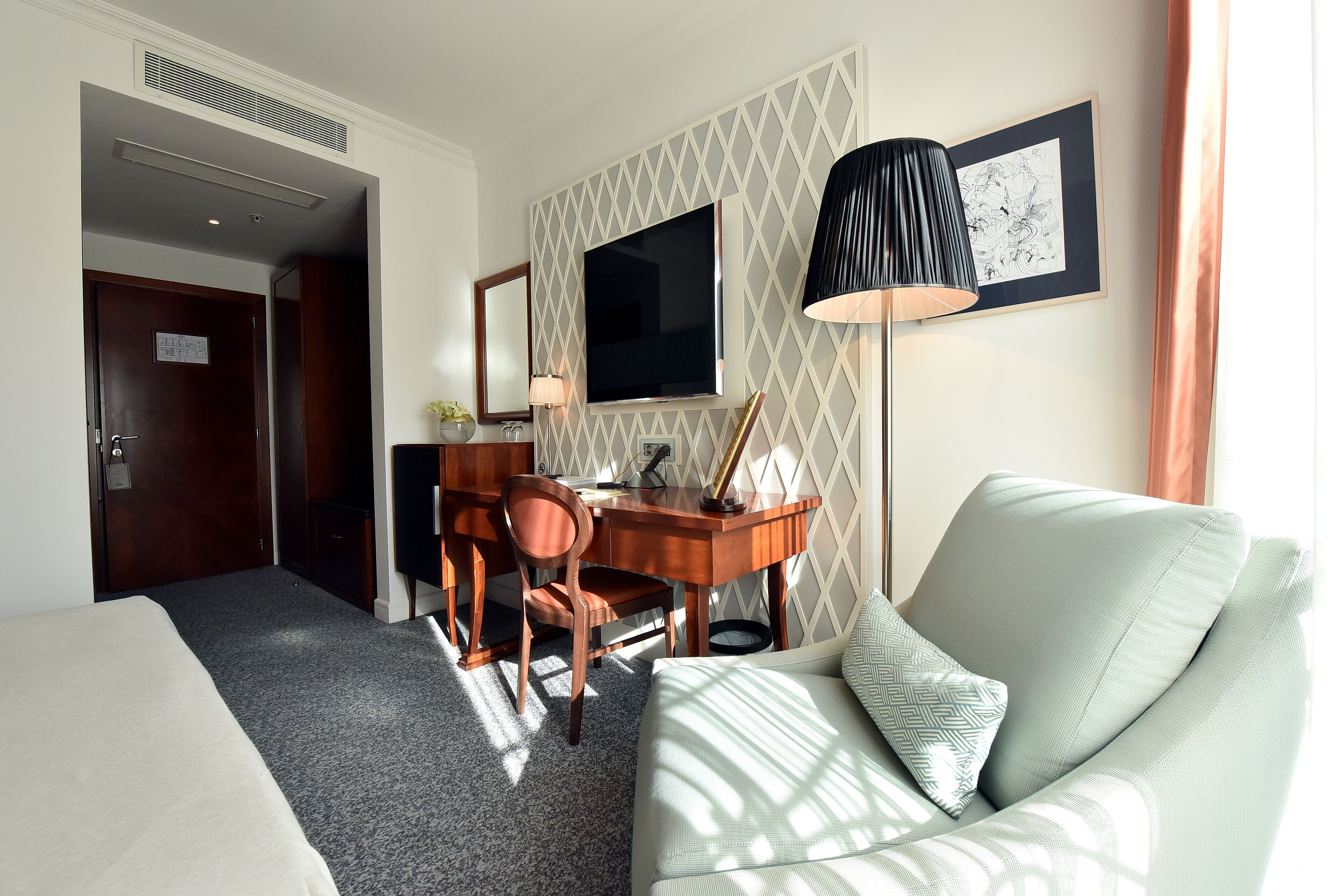 A hotel room with a bed, a desk with a chair, a TV, a lamp, and a couch.
