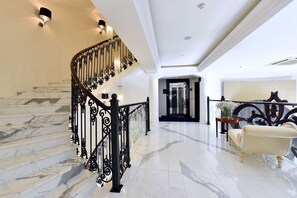 Un escalier en marbre, agrémenté d’une rampe en fer forgé noir, mène à un palier.