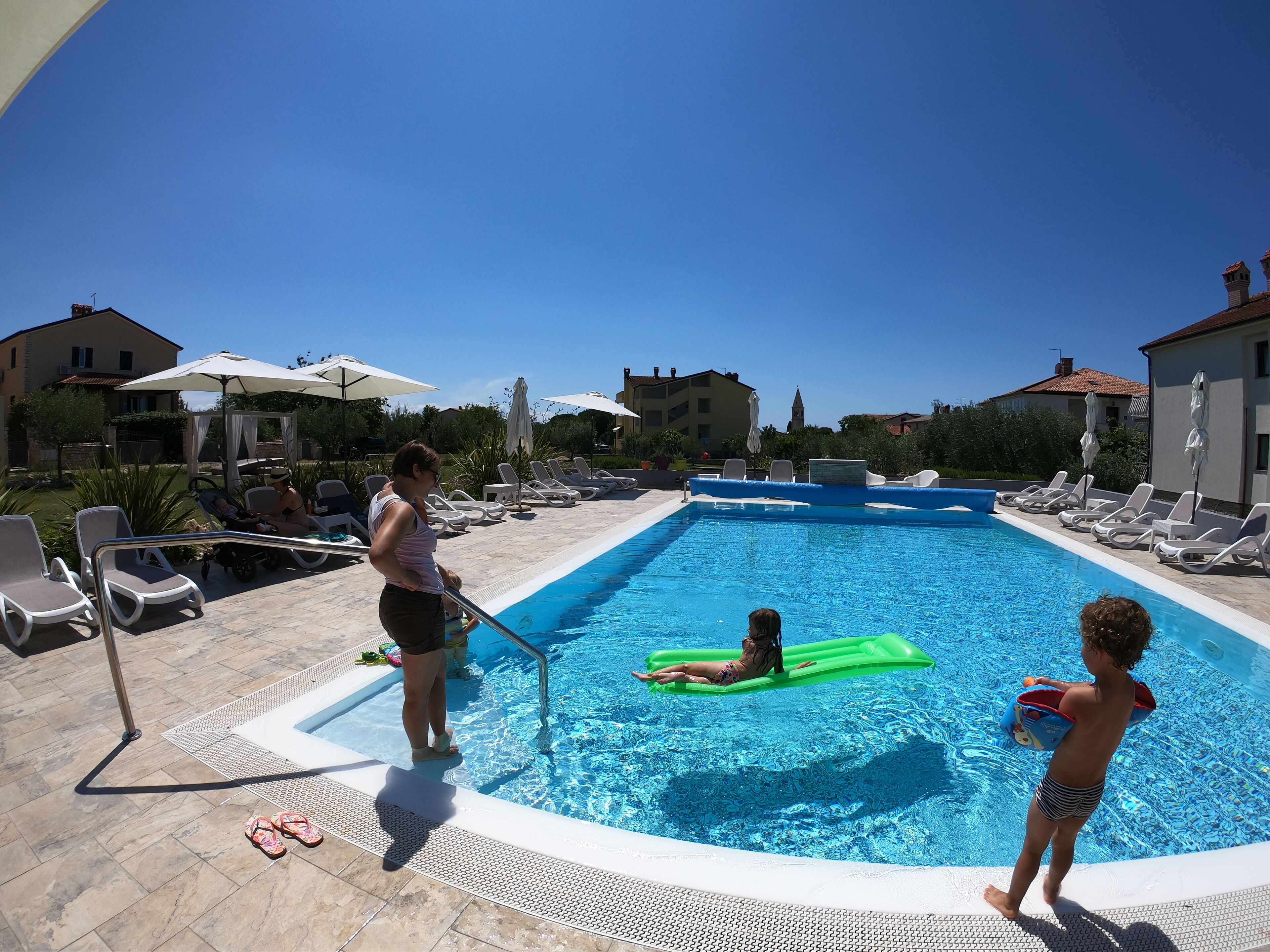 Una piscina con sillas de descanso y sombrillas, rodeada de edificios.