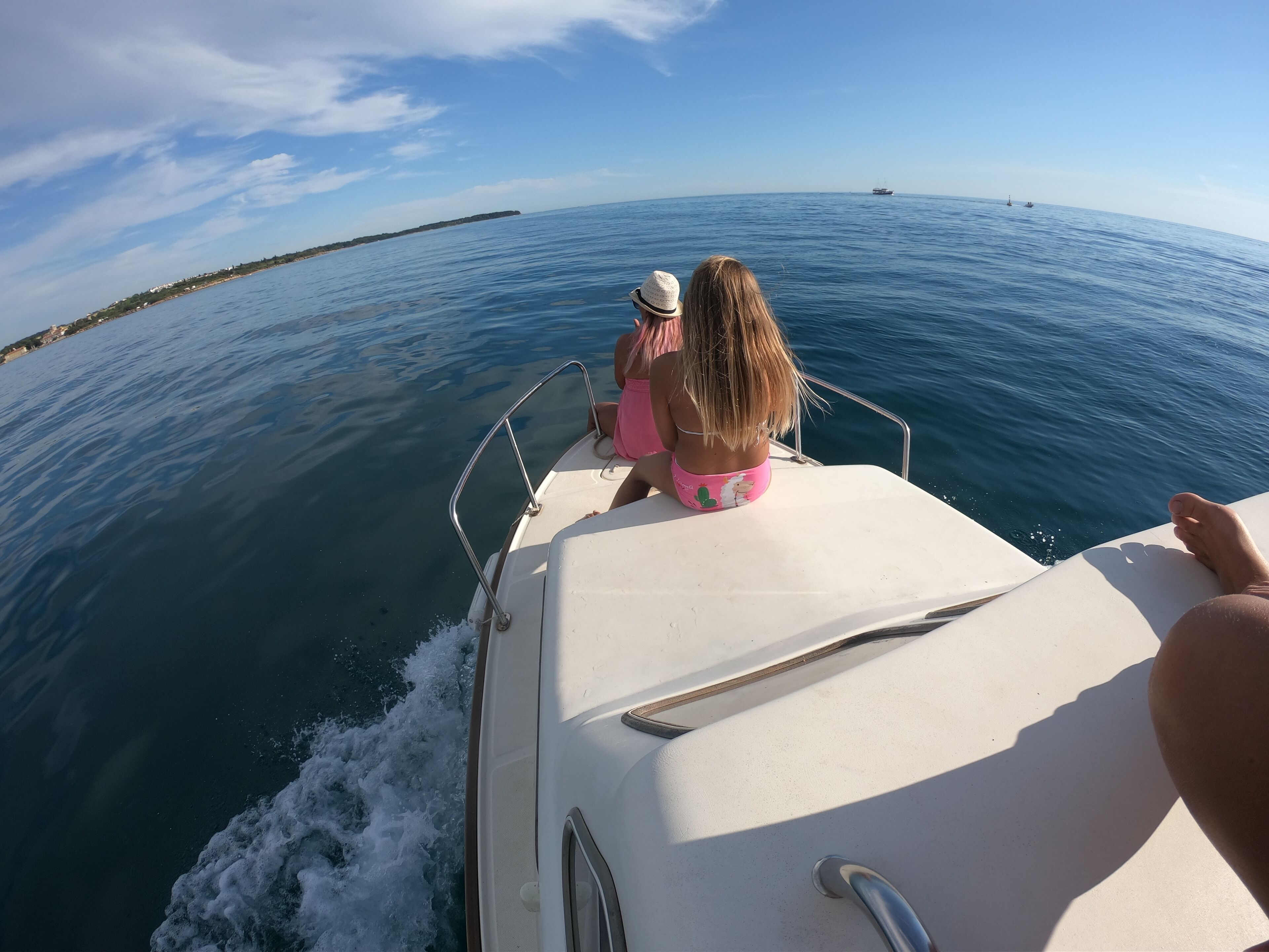 A boat with a person wearing a hat and pink shorts, another person in a bikini, and a third person in the foreground.