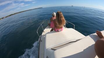 A boat with a person wearing a hat and pink shorts, another person in a bikini, and a third person in the foreground.