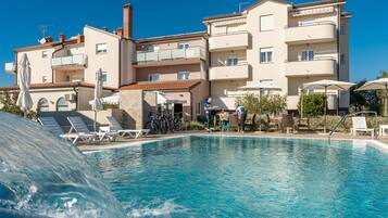 Una piscina con sillones de descanso y sombrillas, rodeada de edificios de varios pisos con balcones.