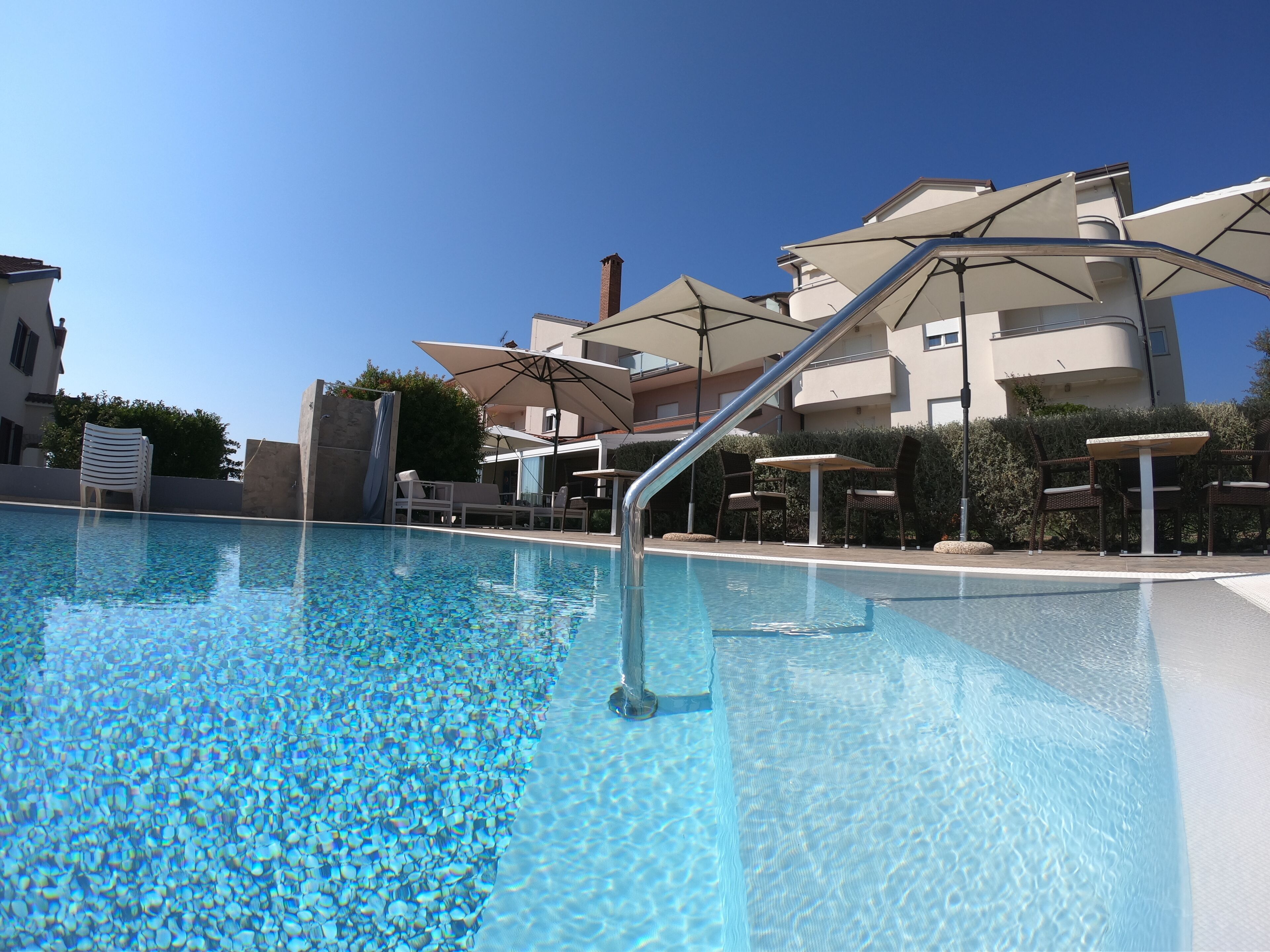 A swimming pool with clear water, surrounded by lounge chairs and umbrellas.