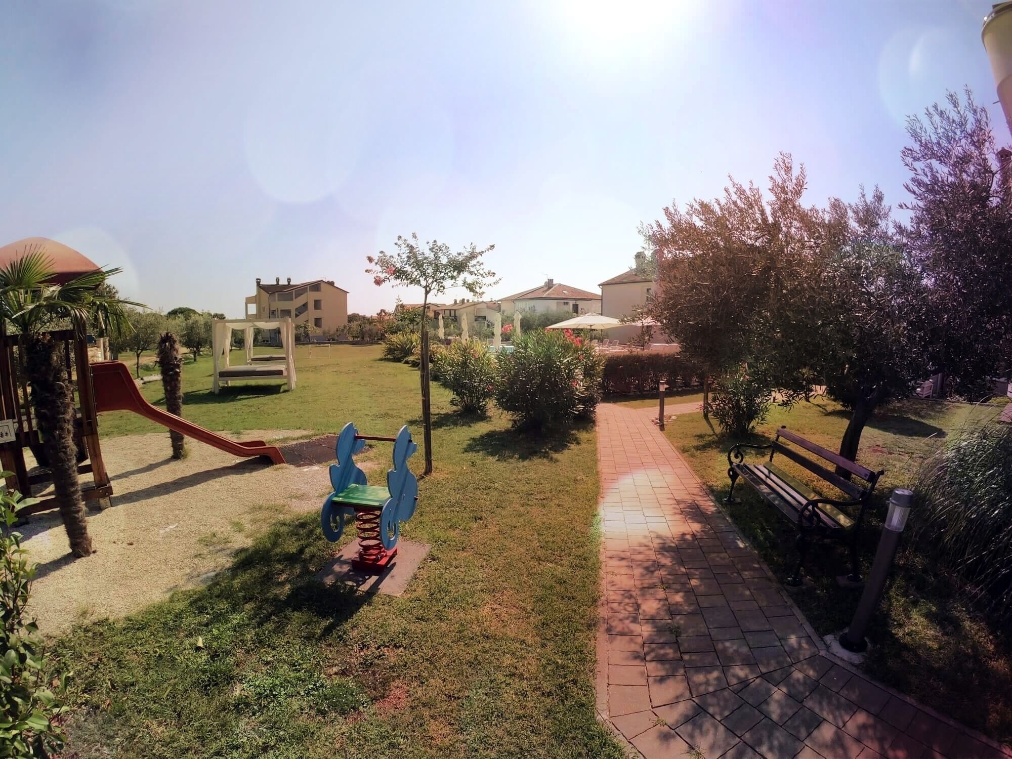 A playground with a slide and swings, a brick pathway, and a bench.