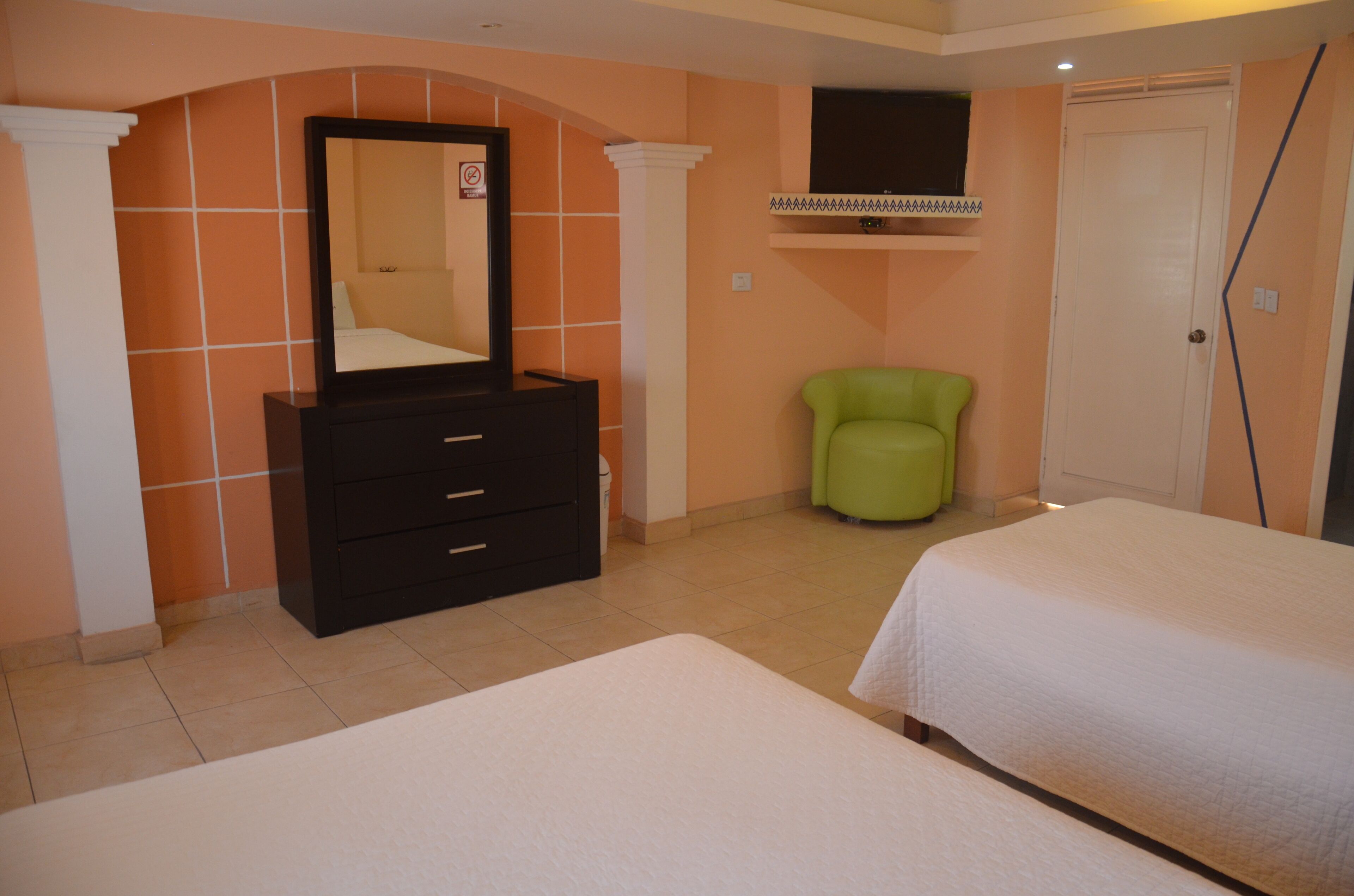 A bedroom with two beds, a dresser, a green chair, and a door.