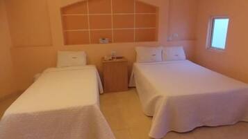 A hotel room with two single beds, a small bedside table with a lamp, and a window providing natural light.
