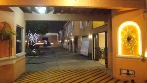 A narrow alleyway with a wooden ceiling and a light fixture. There are buildings on either side, and a vehicle is parked in the distance.