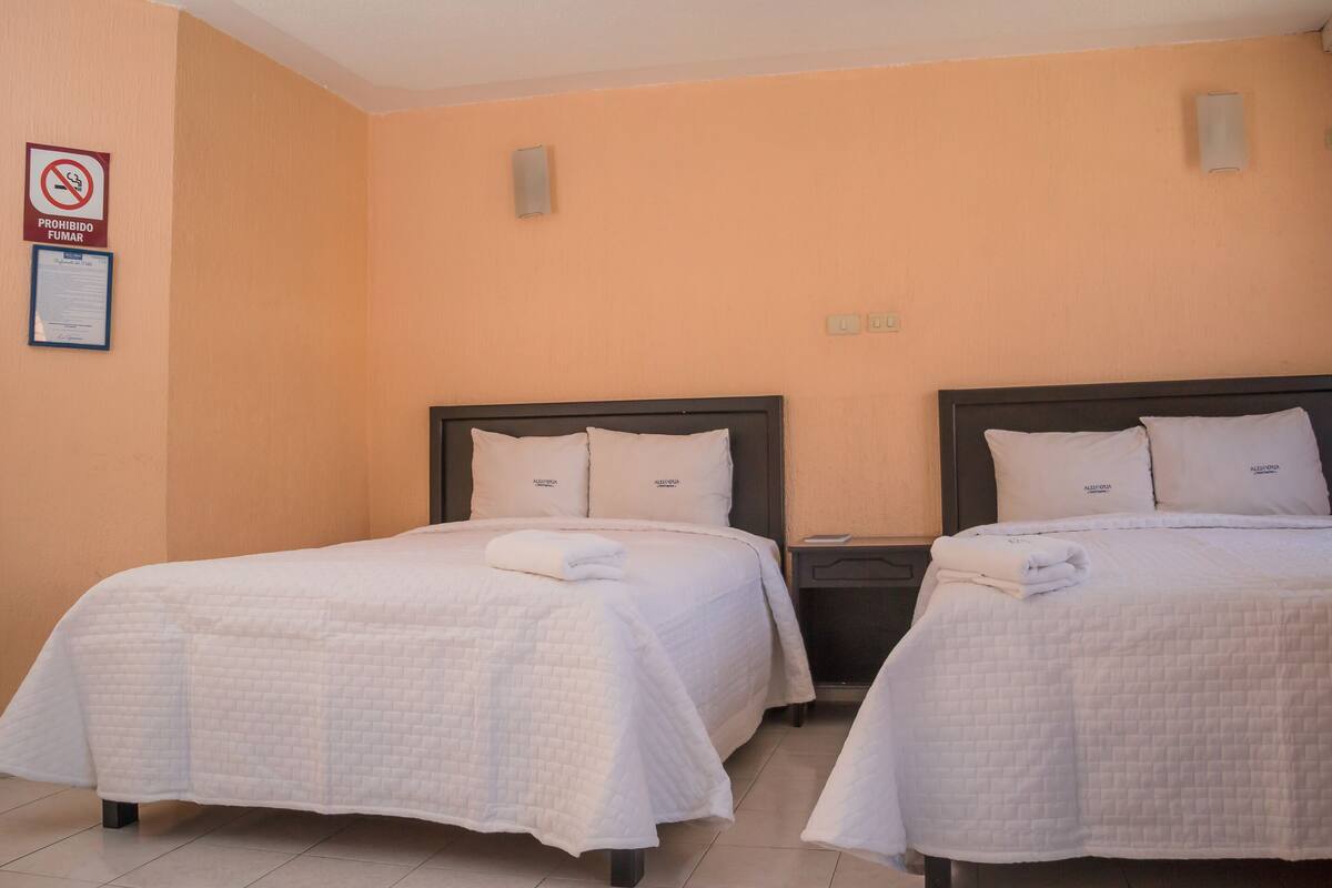 Ein Hotelzimmer mit zwei Betten, jeweils mit weiß gestopfter Bettdecke und passenden Kissen. An der Wand ist ein Telefon und es gibt ein Fenster mit Blick nach außen.