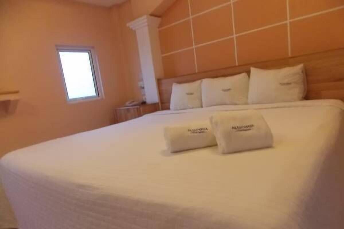 Ein Hotelzimmer mit einem großen Bett, einem Fenster und einer Fliesenwand.