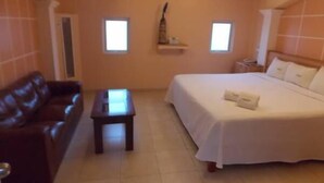 A hotel room with a bed, a brown leather sofa, a small table, and two windows.