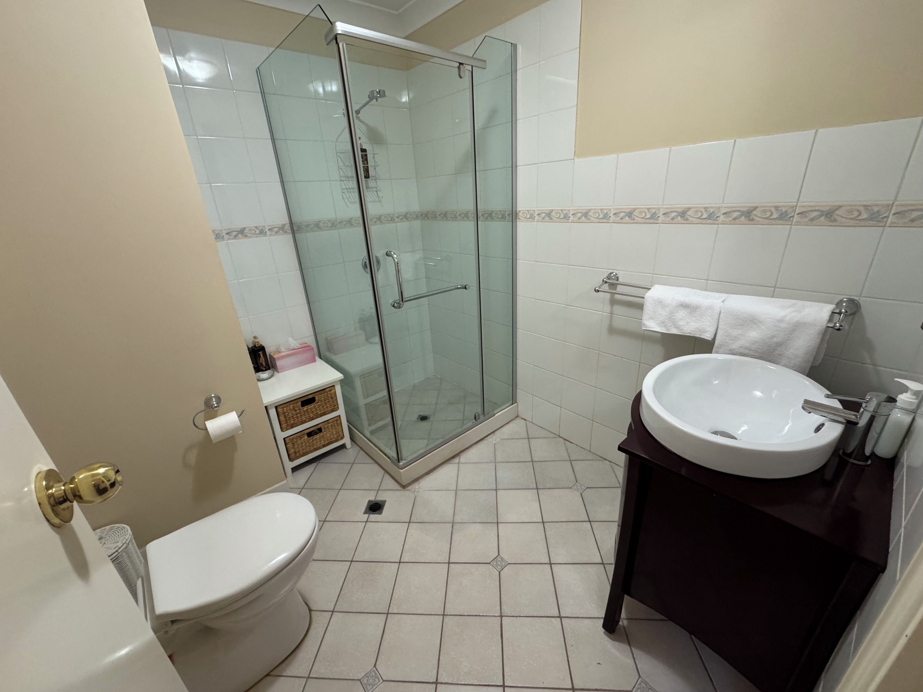 A bathroom with a toilet, a glass-enclosed shower, a sink, and a towel rack.