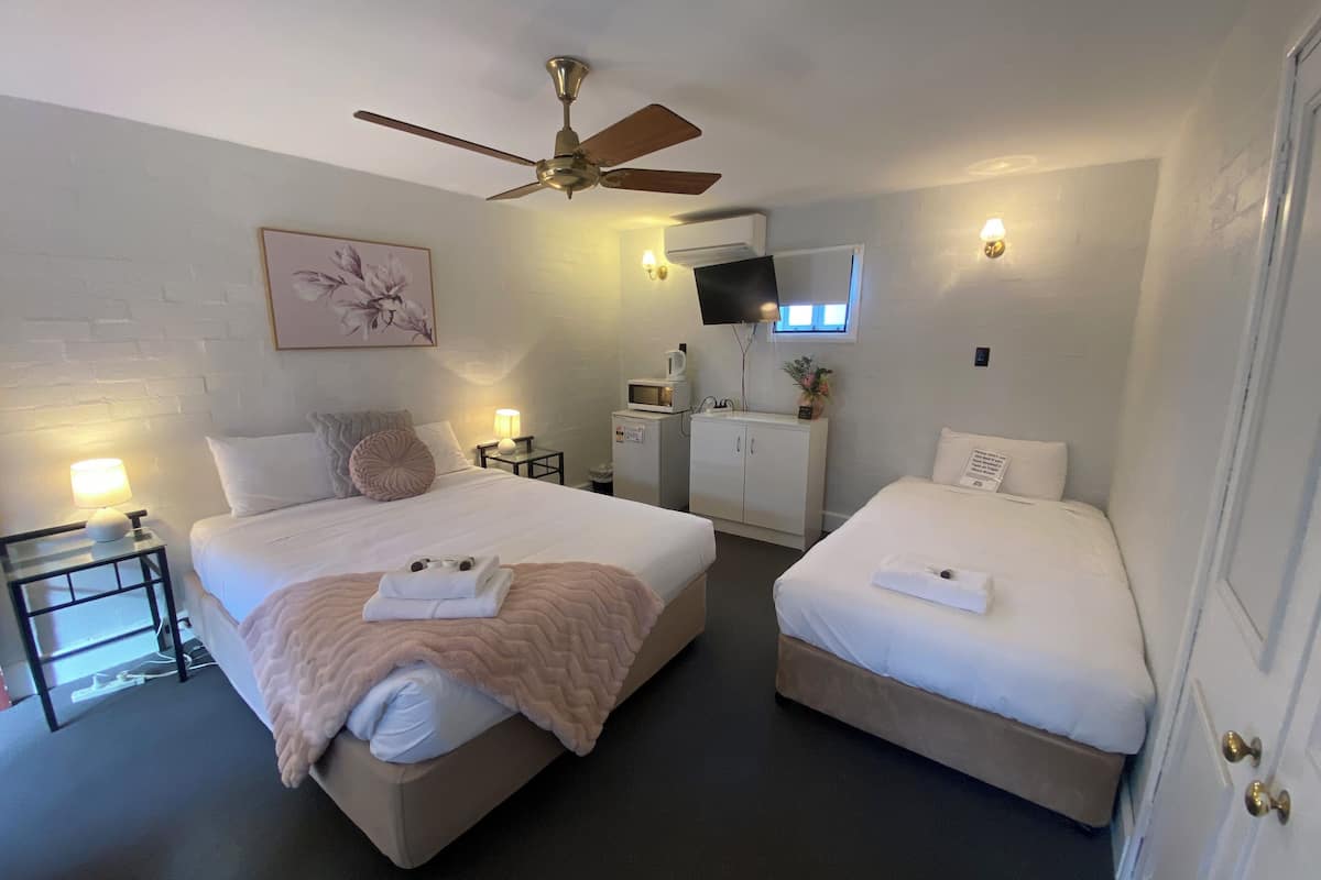 A hotel room with two beds, a ceiling fan, a TV, a small kitchenette, and a window.