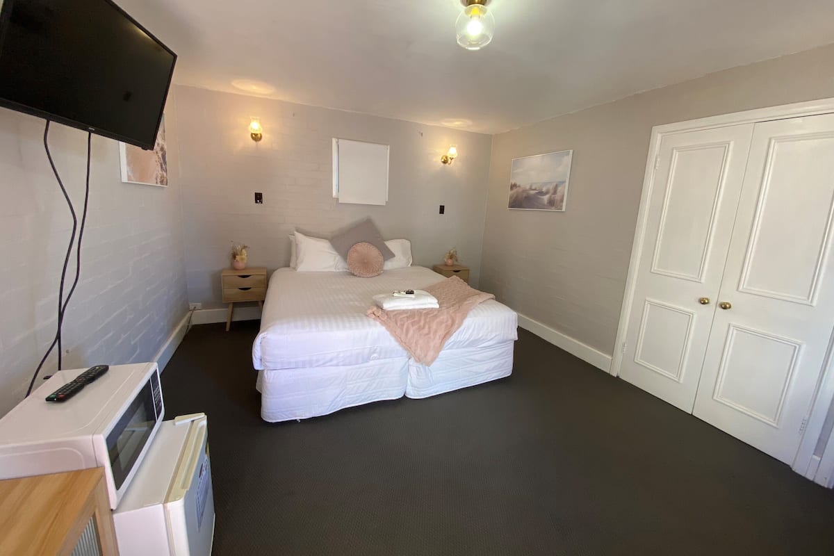 A bedroom with a bed, bedside tables, a TV, a microwave, and a wardrobe.