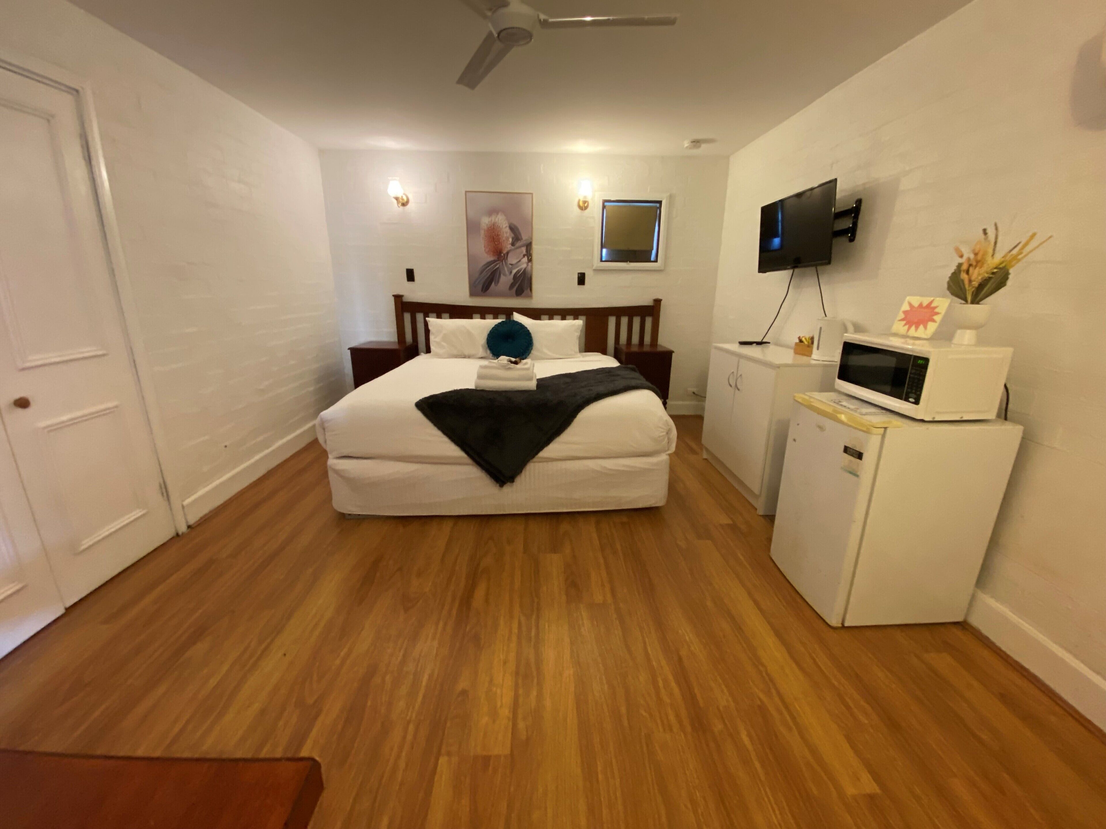 A bedroom with a bed, a television, a microwave, and a small cabinet.
