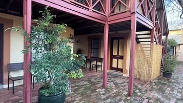 A covered patio area with a brick floor, a large potted plant, a wooden bench, and a table.