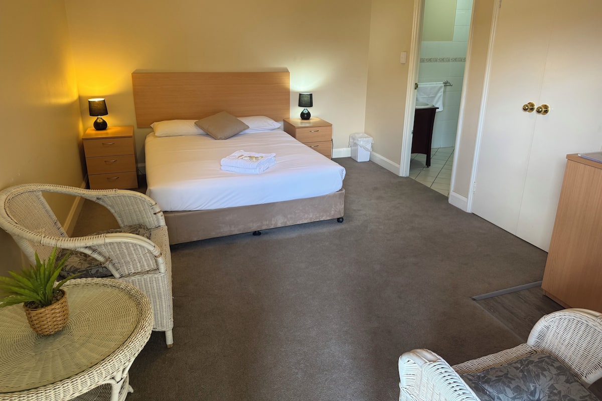 A neatly arranged bedroom with a bed, bedside tables, a chair, and a small table with a plant.