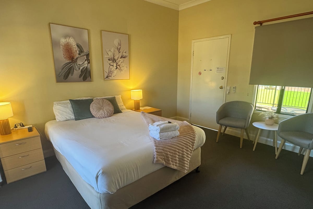 A hotel room with a large bed, bedside lamps, a desk, a chair, and two wall-mounted flower paintings.