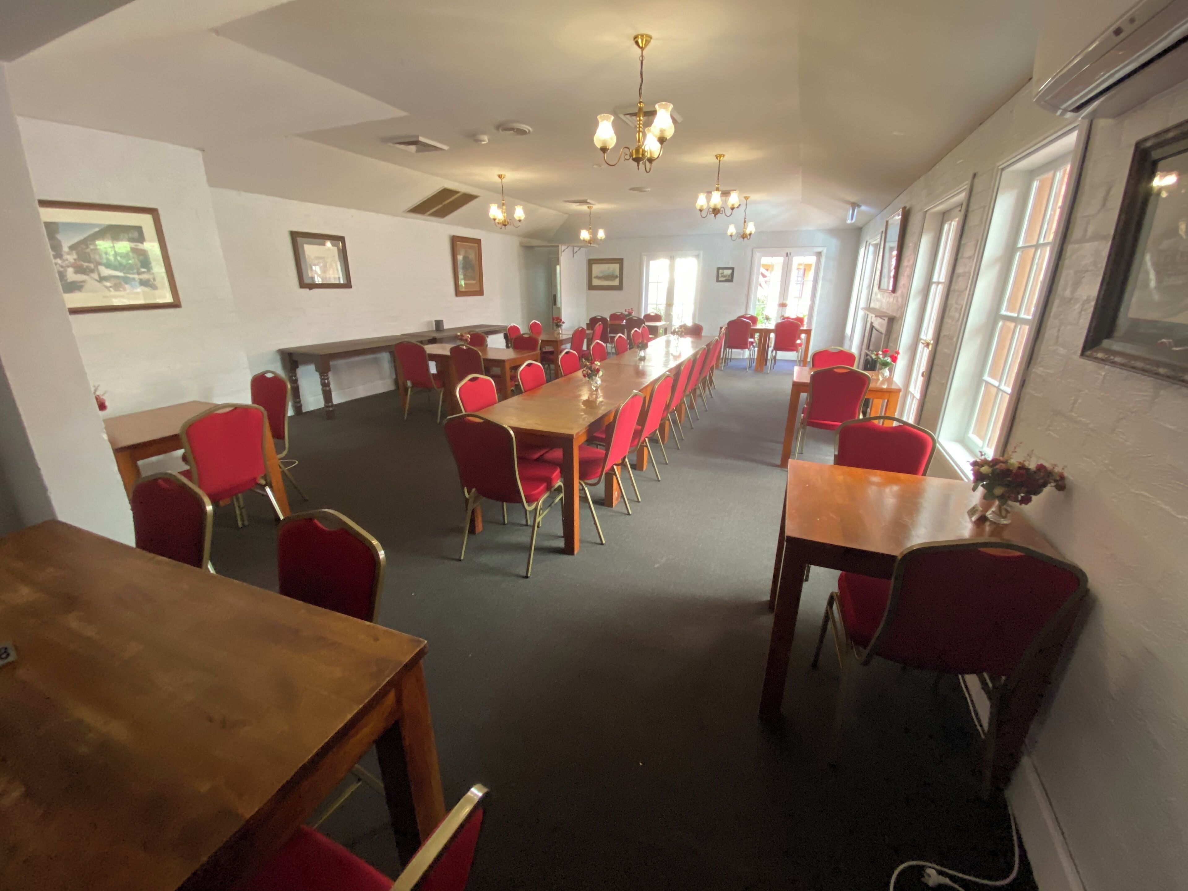 Une salle de conférence avec de longues tables et des chaises rouges, de grandes fenêtres et des luminaires au plafond.