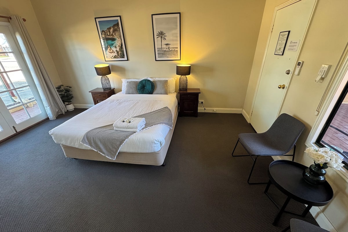 A hotel room with a large bed, two bedside tables with lamps, a chair, and two framed pictures on the wall.