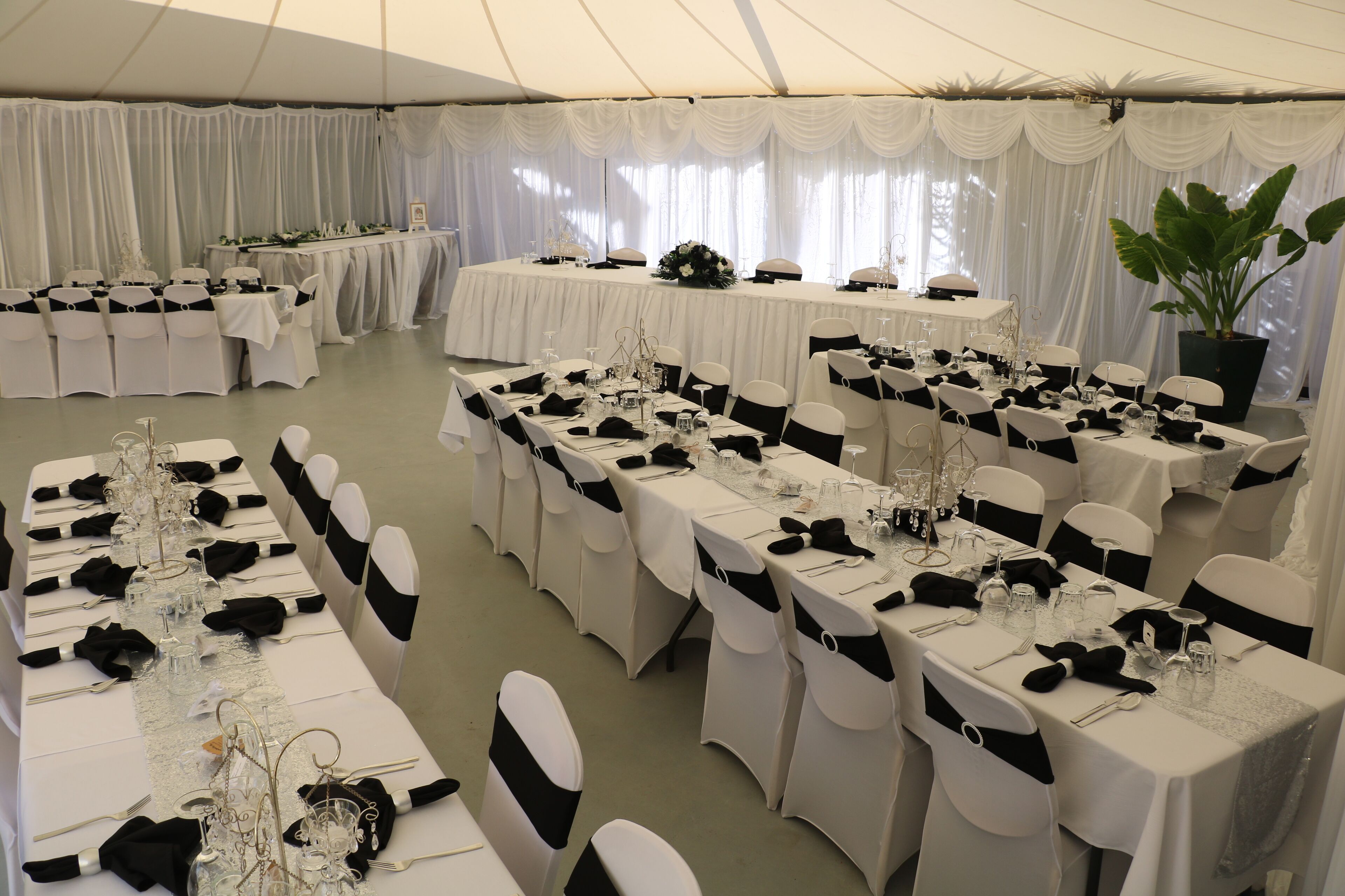 Een tent voor een evenement met meerdere tafels, gedekt voor een formeel diner, met witte tafelkleden, zwarte linten en glazen.