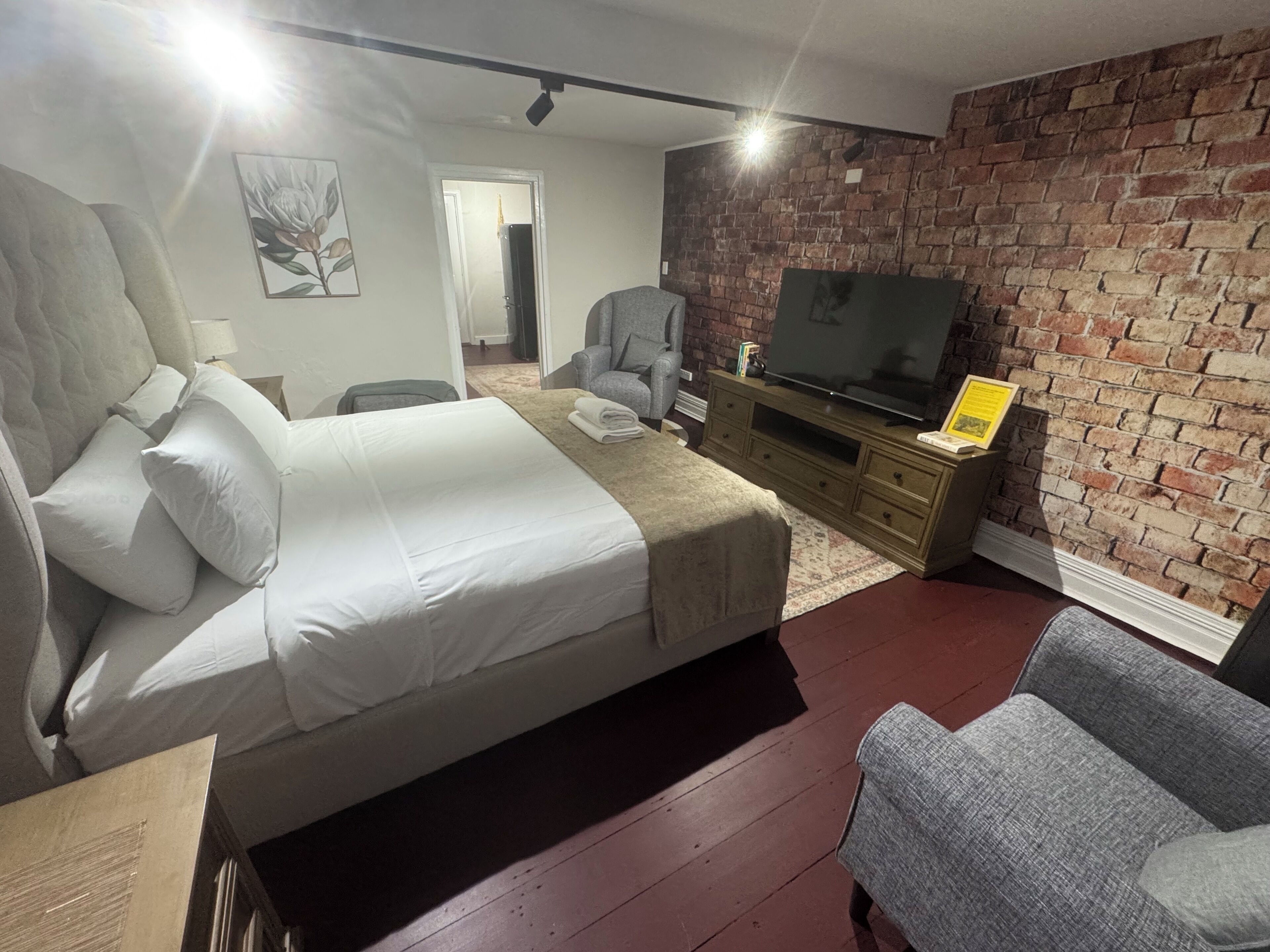 A hotel room with a large bed, a television, a brick wall, and a gray armchair.