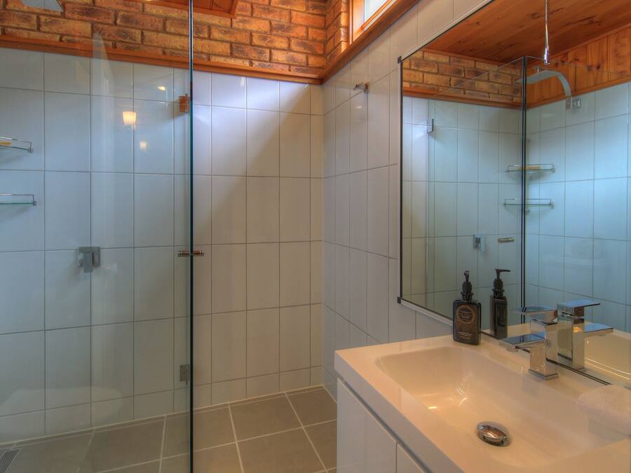 Un baño moderno con cabina de ducha de vidrio, un espejo grande y un lavabo blanco con tocador.