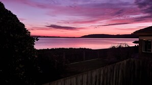 Una vista al atardecer sobre una masa de agua, con una cerca de madera y un edificio en primer plano.