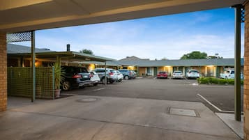 A parking area with multiple cars, a covered walkway, and a building with a green roof.