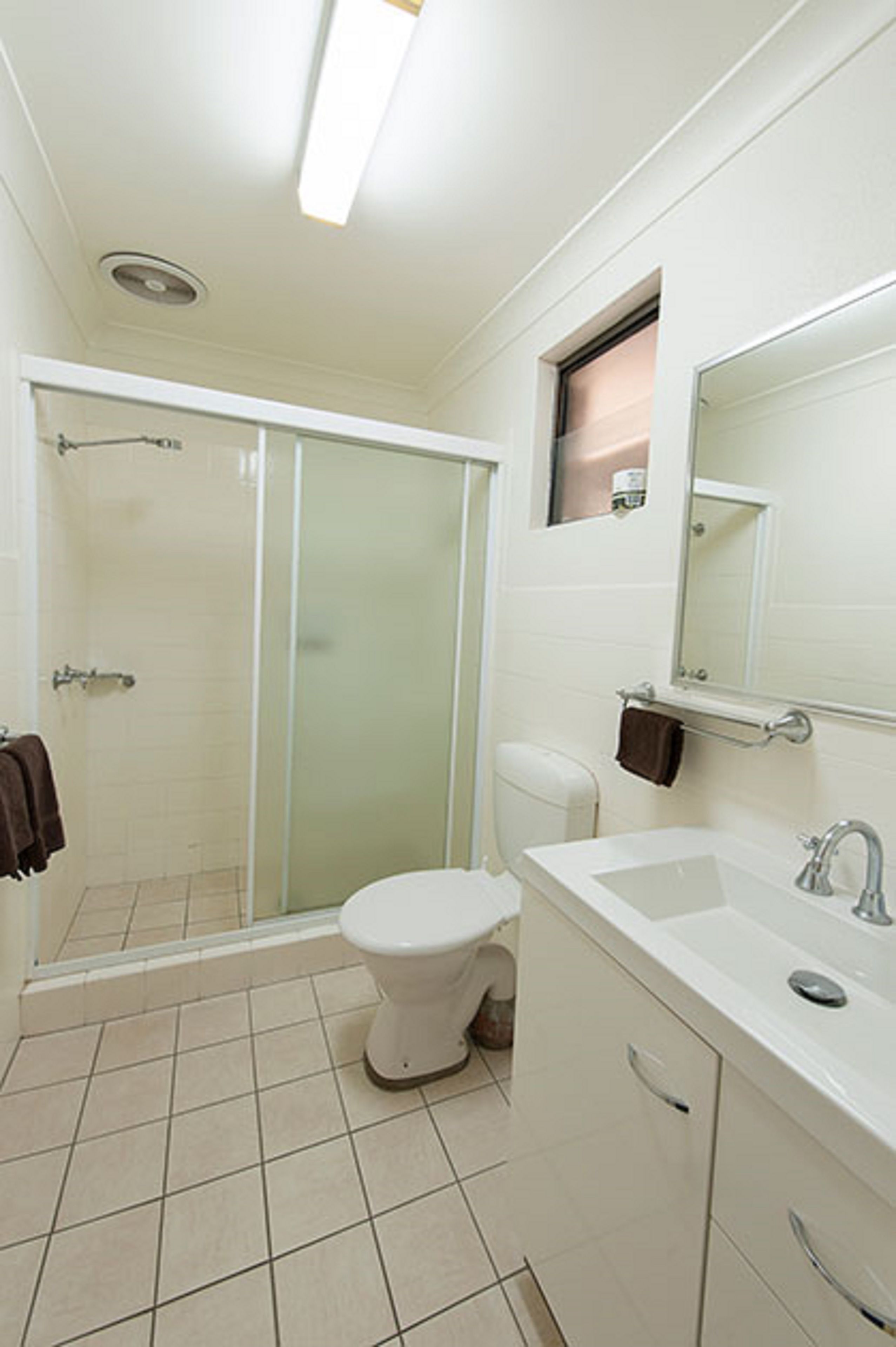 A bathroom with a glass shower enclosure, a toilet, a sink, and a mirror.