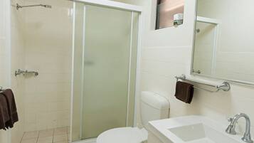 A bathroom with a glass shower enclosure, a toilet, a sink, and a mirror.