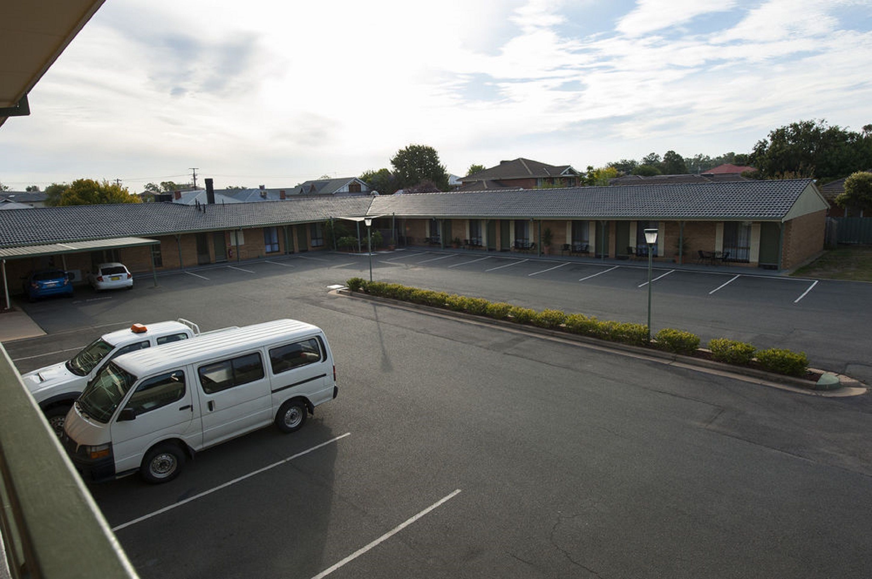 A motel with a parking lot, a covered outdoor seating area, and a building with a tiled roof.
