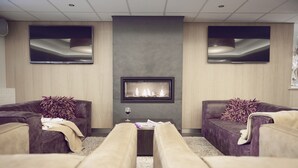 A modern lounge with two sofas, a fireplace, and a flat-screen TV. - Aparthotel Delden (Delden)