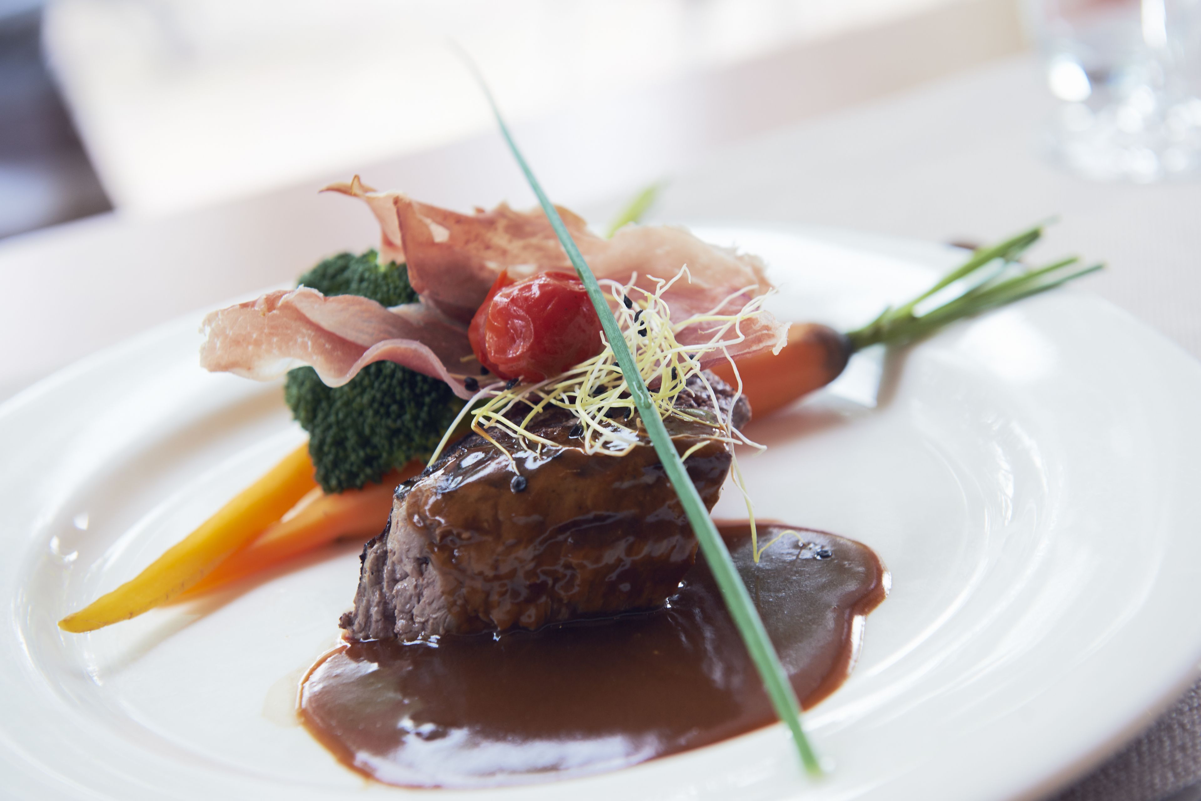 A plate of food with a piece of meat, vegetables, and a garnish.