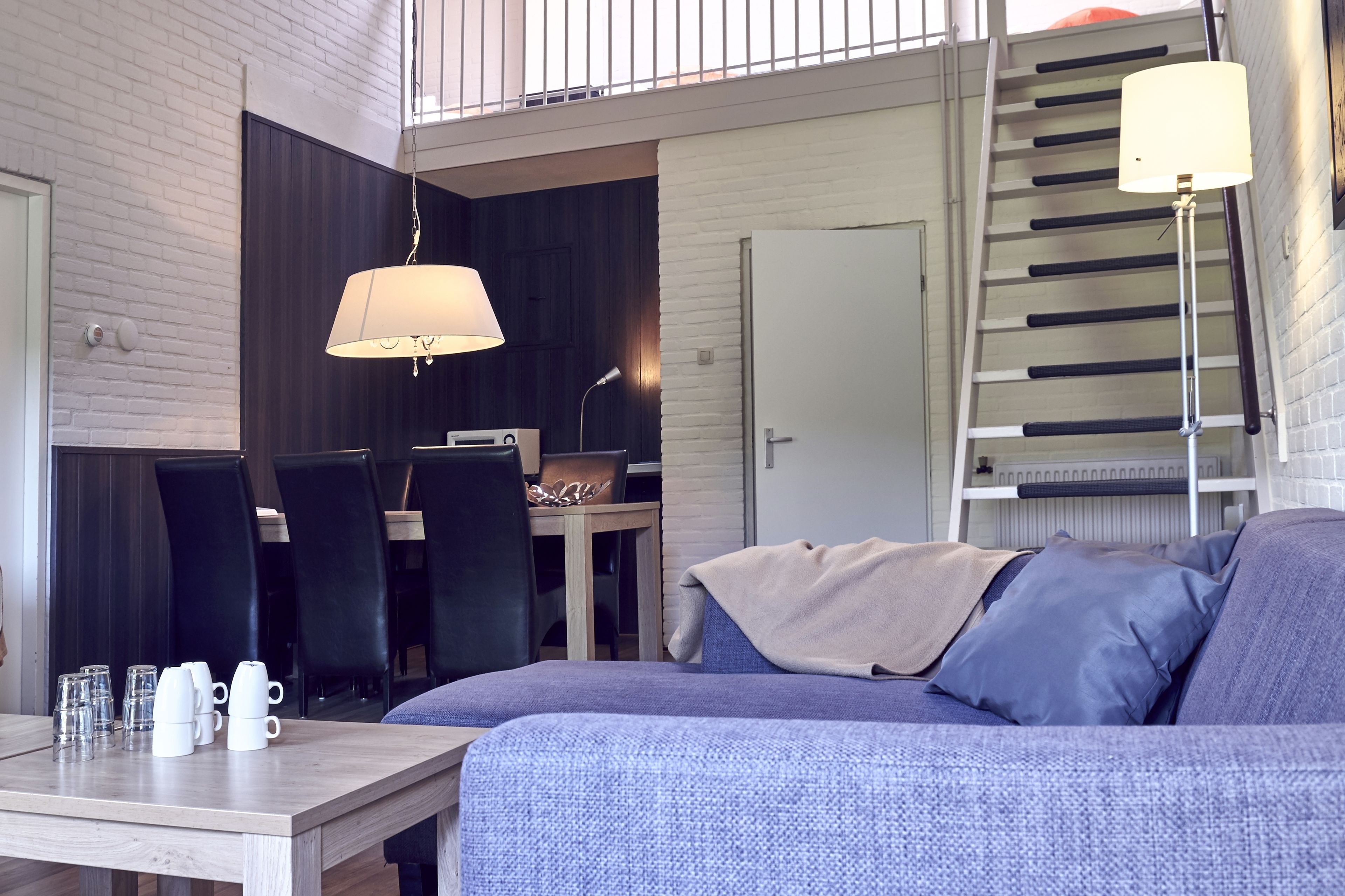 A modern living area with a sofa, a dining table with chairs, and a staircase.