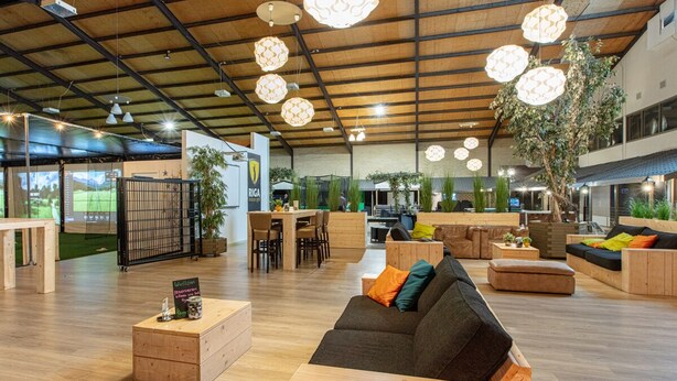 A spacious indoor area with wooden flooring, a black sofa, wooden tables, and hanging spherical lights. - Aparthotel Delden (Delden)