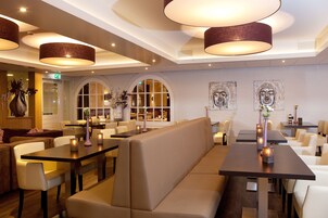 Interior de restaurante moderno com mesas altas, assentos acolchoados e iluminação pendente.