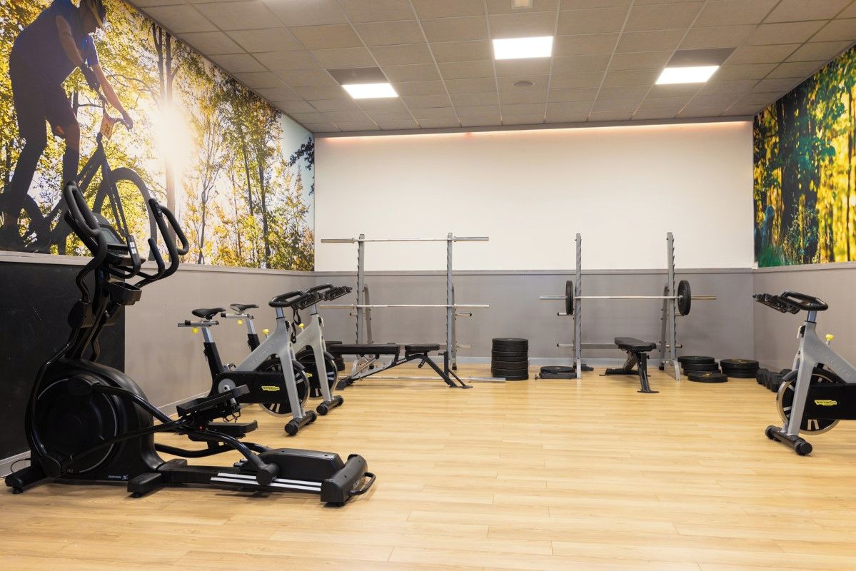Un gimnasio con equipo de ejercicio, un mural en la pared y suelo de madera.