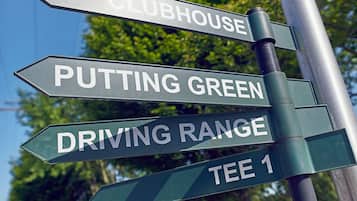 Una señal direccional con múltiples flechas indicando diferentes direcciones, etiquetada con destinos como 'CLUBHOUSE', 'PUTTING GREEN', 'DRIVING RANGE' y 'TEE 1'.