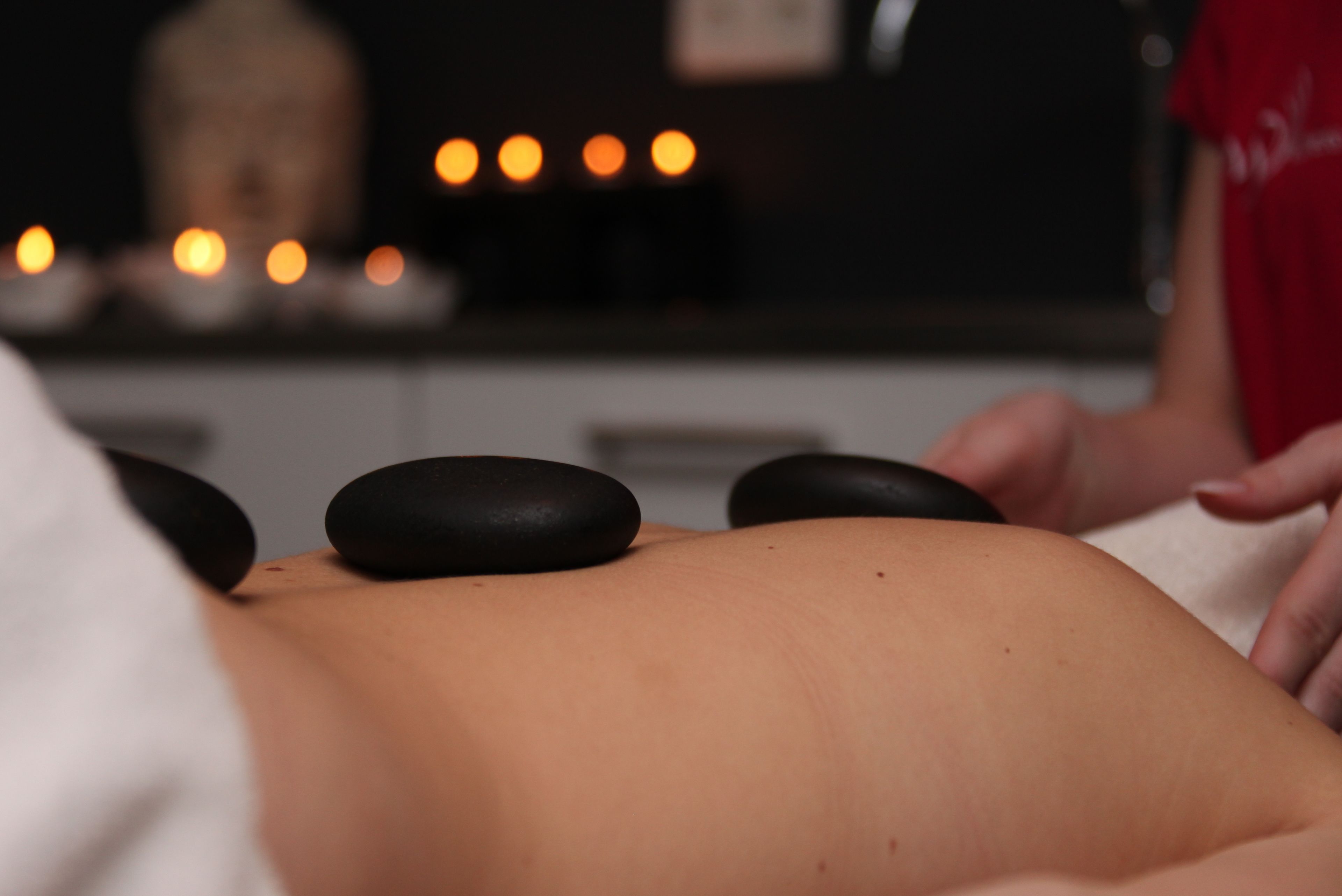 Sesión de terapia de masajes con una persona recibiendo un masaje en la espalda, una estatua de Buda y velas al fondo.