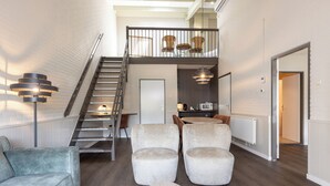 A spacious living area with a staircase leading to a loft, a sofa, armchairs, and a dining area with a table and chairs. - Aparthotel Delden (Delden)