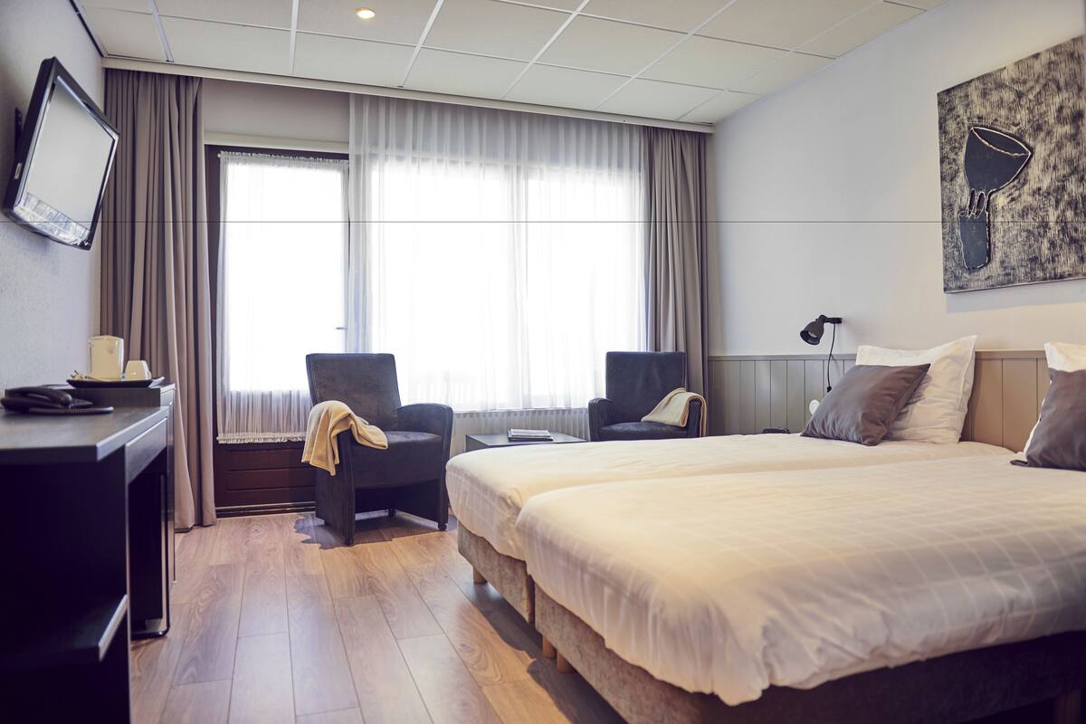 Ein Hotelzimmer mit einem großen Bett, zwei Sesseln, einem Schreibtisch und einem Fernseher.