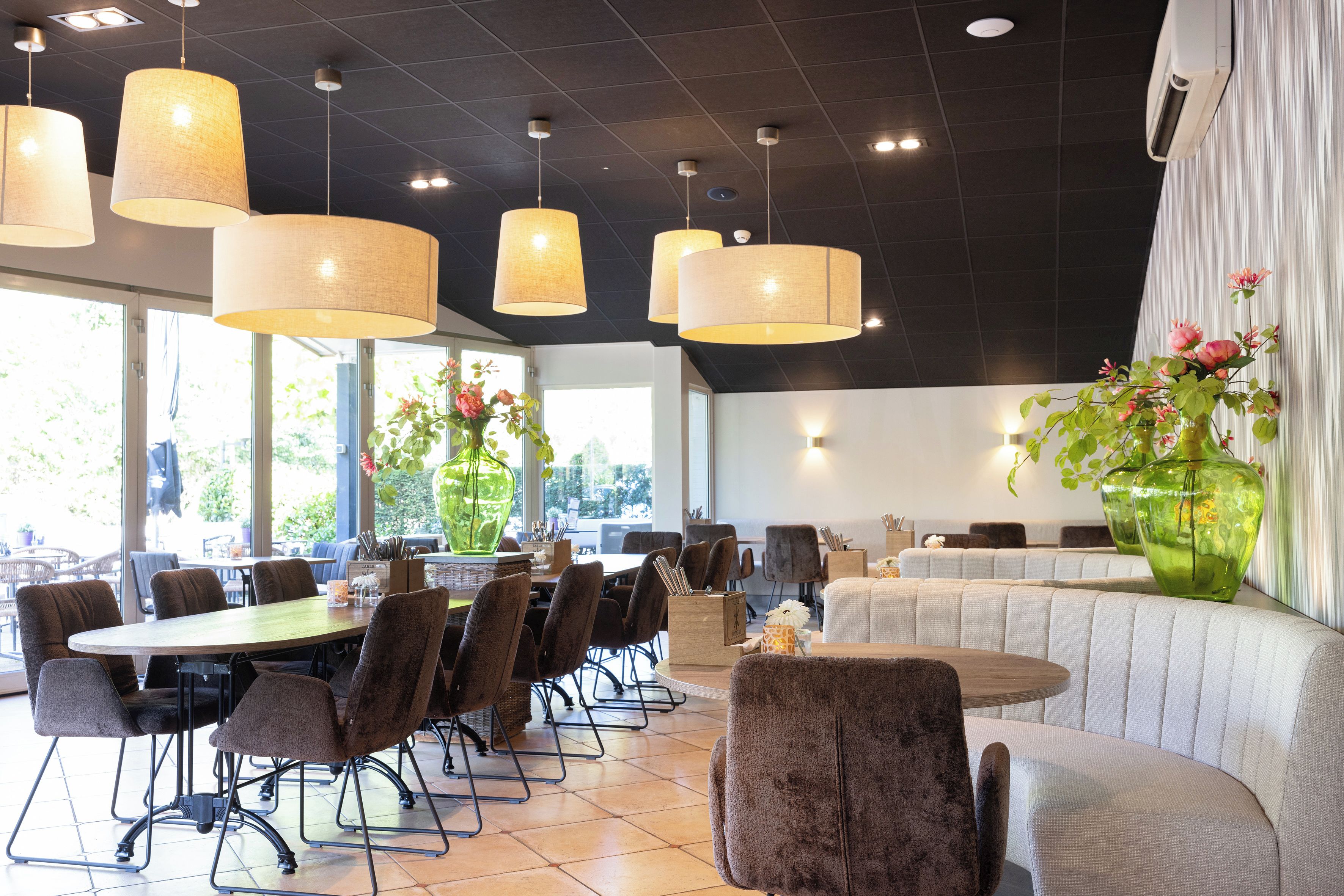 En restaurang med många bord och stolar, stora hängande lampor och en stor vas med blommor.