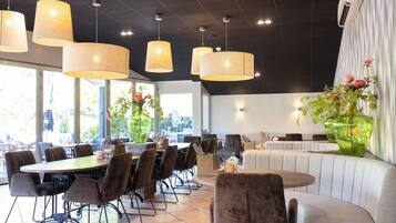 En restaurang med många bord och stolar, stora hängande lampor och en stor vas med blommor.
