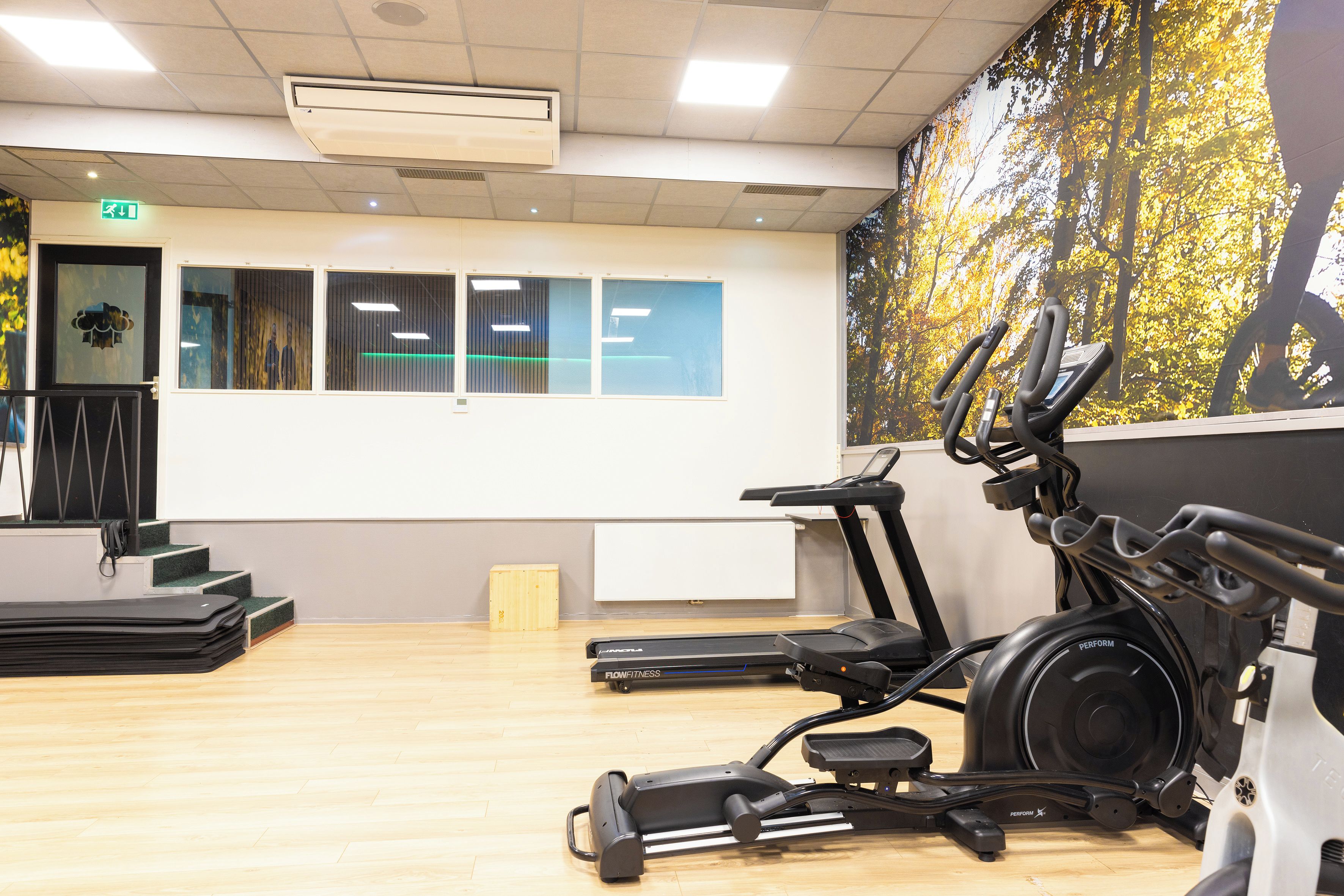 Un gimnasio con equipo de ejercicio, una pared con cuadros enmarcados y una escalera.