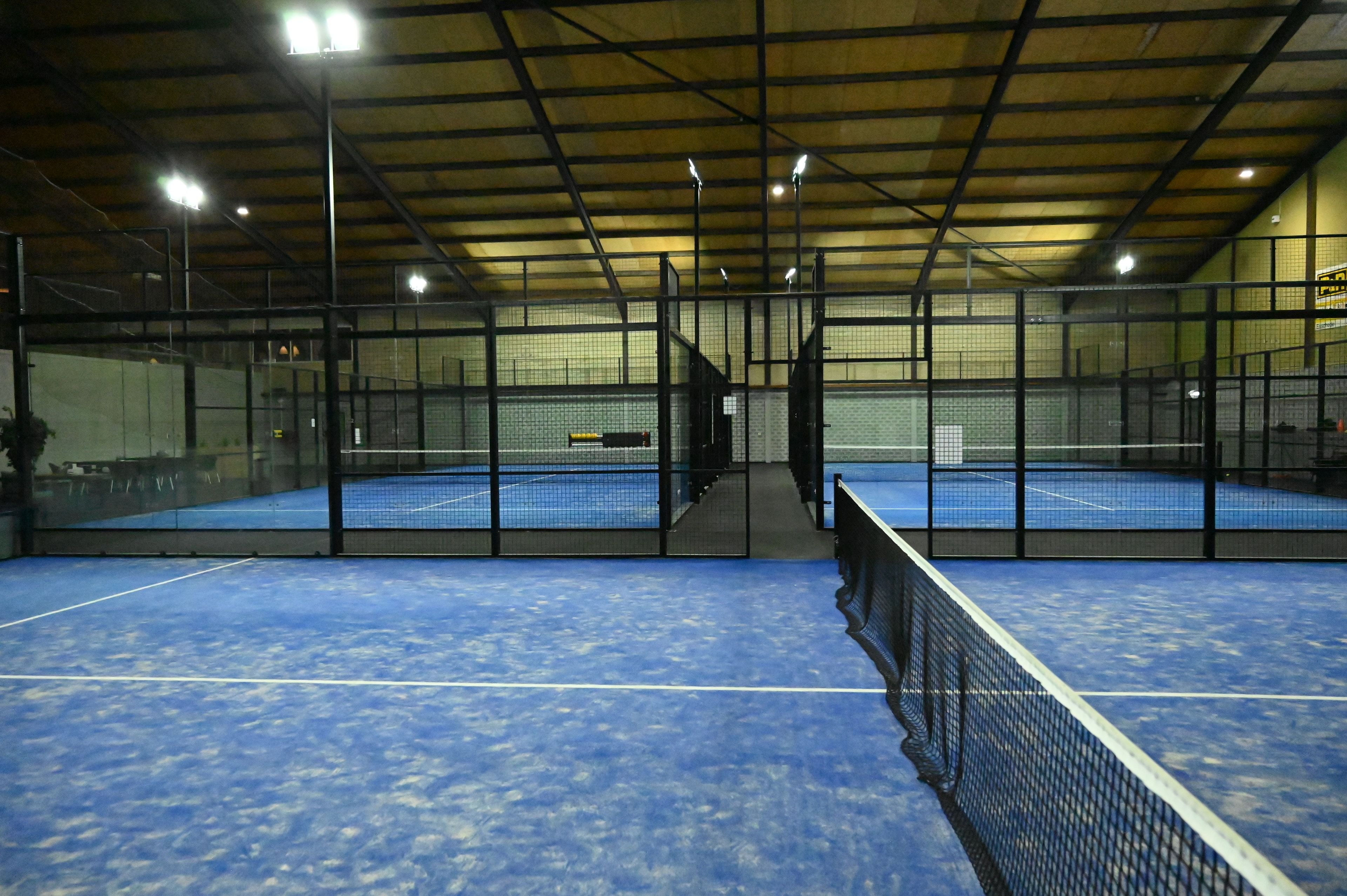 Una cancha de tenis interior con red, delimitada por paredes y techo.