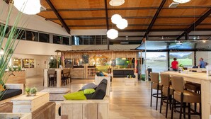 A spacious, modern lounge area with wooden furniture, a bar, and a view of a golf course. - Aparthotel Delden (Delden)